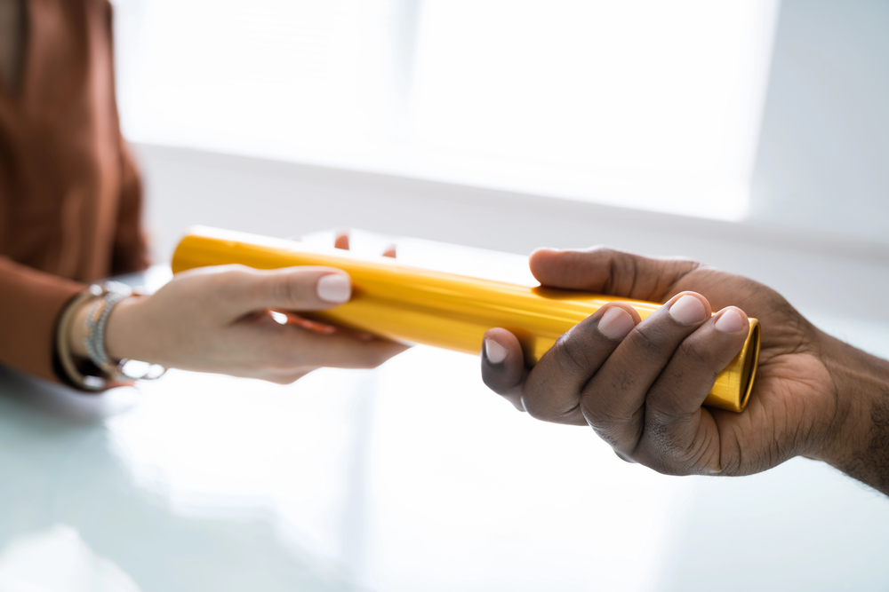 Close up of one person handing a baton over to another symbolising giving ownership